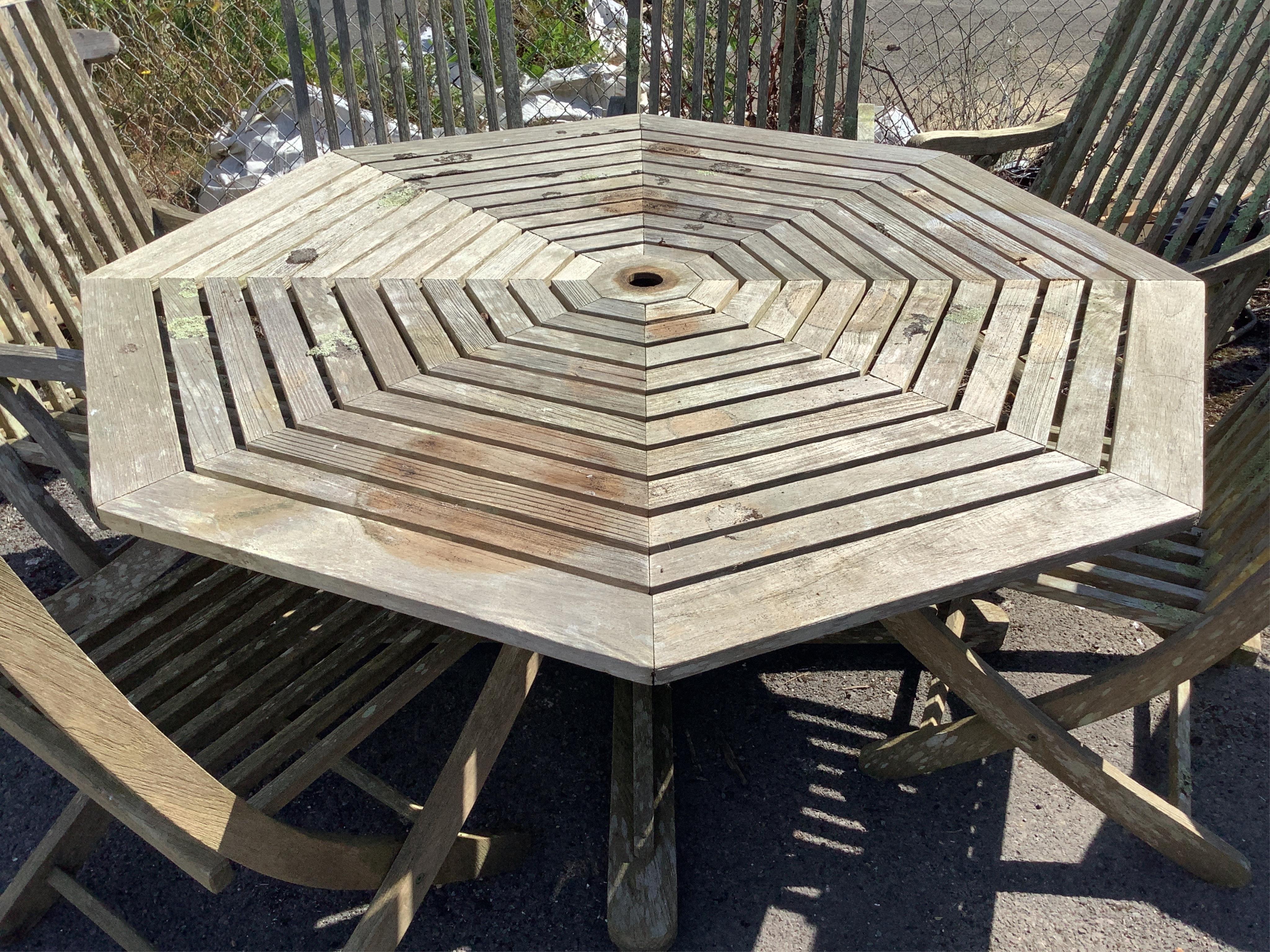 A weathered teak octagonal garden table, width 159cm, height 72cm, together with eight slatted teak folding garden chairs, four with arms. Condition - fair